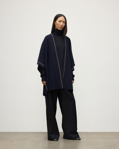 MODEL WEARS JOHNSTONS OF ELGIN WOMENS HAWK PONCHO NAVY 100% CASHMERE OVER NAVY ROLL NECK SWEATER AND NAVY TROUSERS KAU05769Q25973O/S