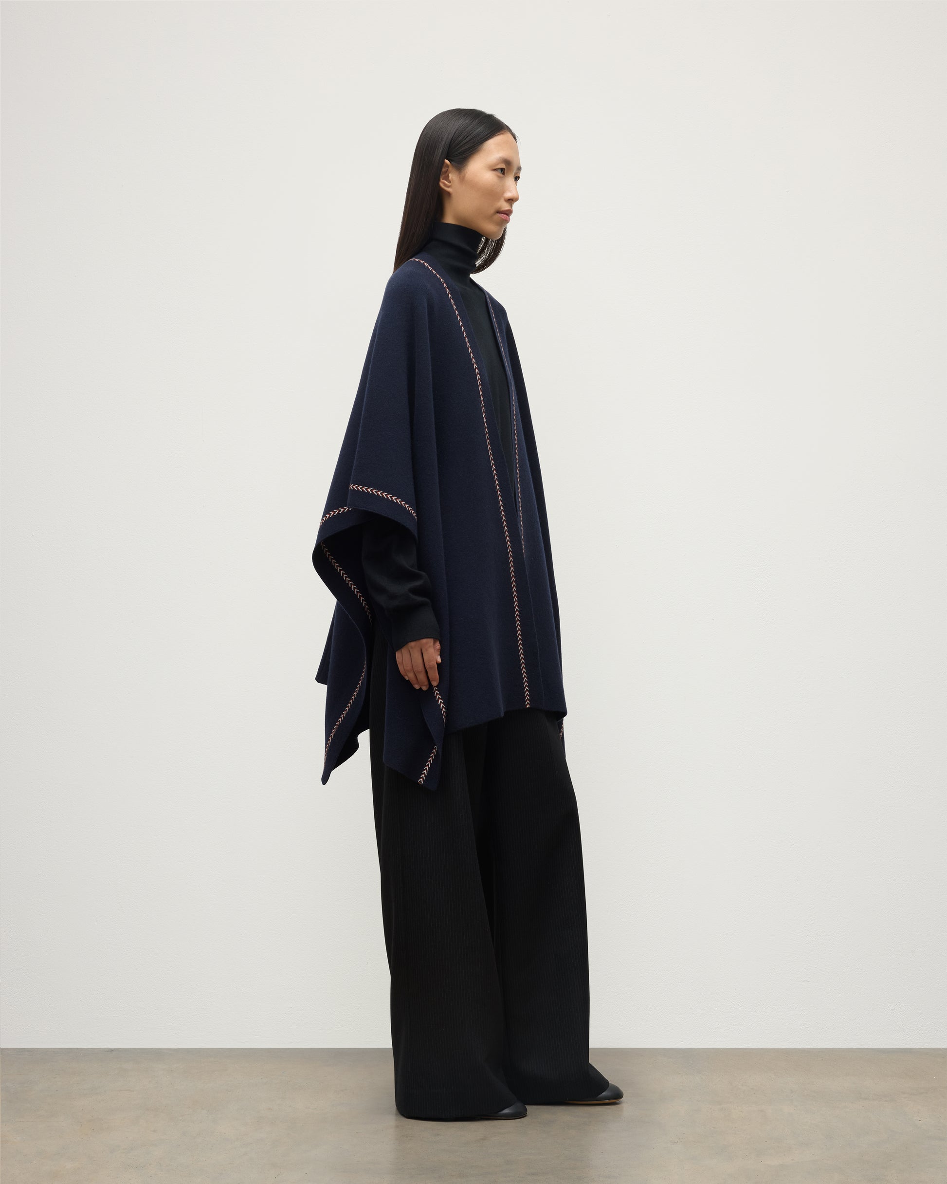 MODEL WEARS JOHNSTONS OF ELGIN WOMENS HAWK PONCHO NAVY 100% CASHMERE OVER NAVY ROLL NECK SWEATER AND NAVY TROUSERS KAU05769Q25973O/S