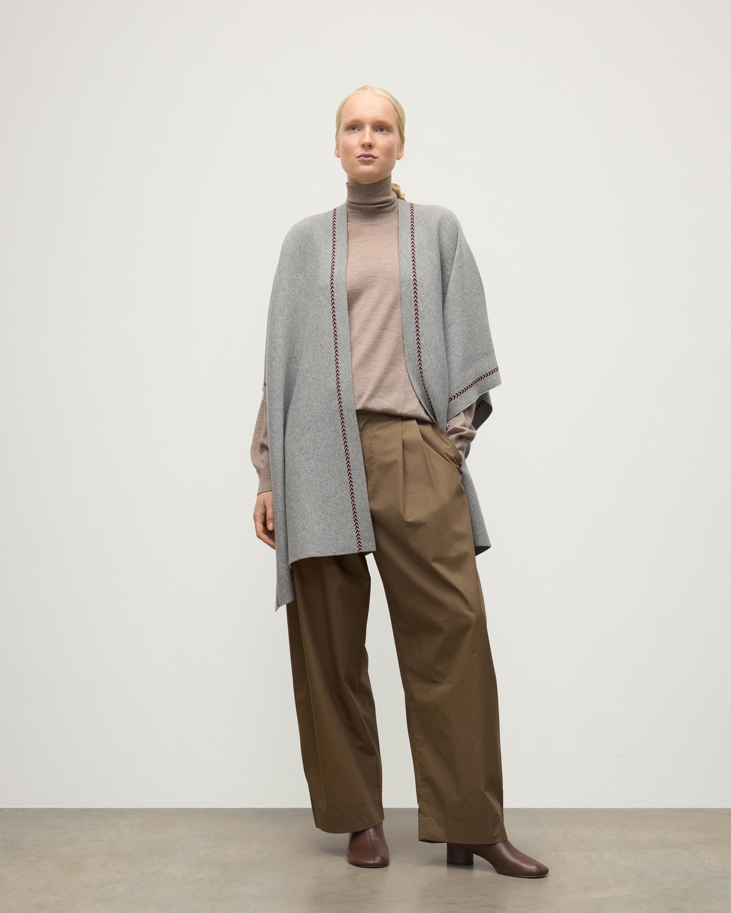 MODEL WEARS JOHNSTONS OF ELGIN WOMENS HAWK PONCHO LIGHT GREY 100% CASHMERE OVER A NATURAL CASHMERE SWEATER AND BROWN TROUSERS KAU05769Q25974O/S
