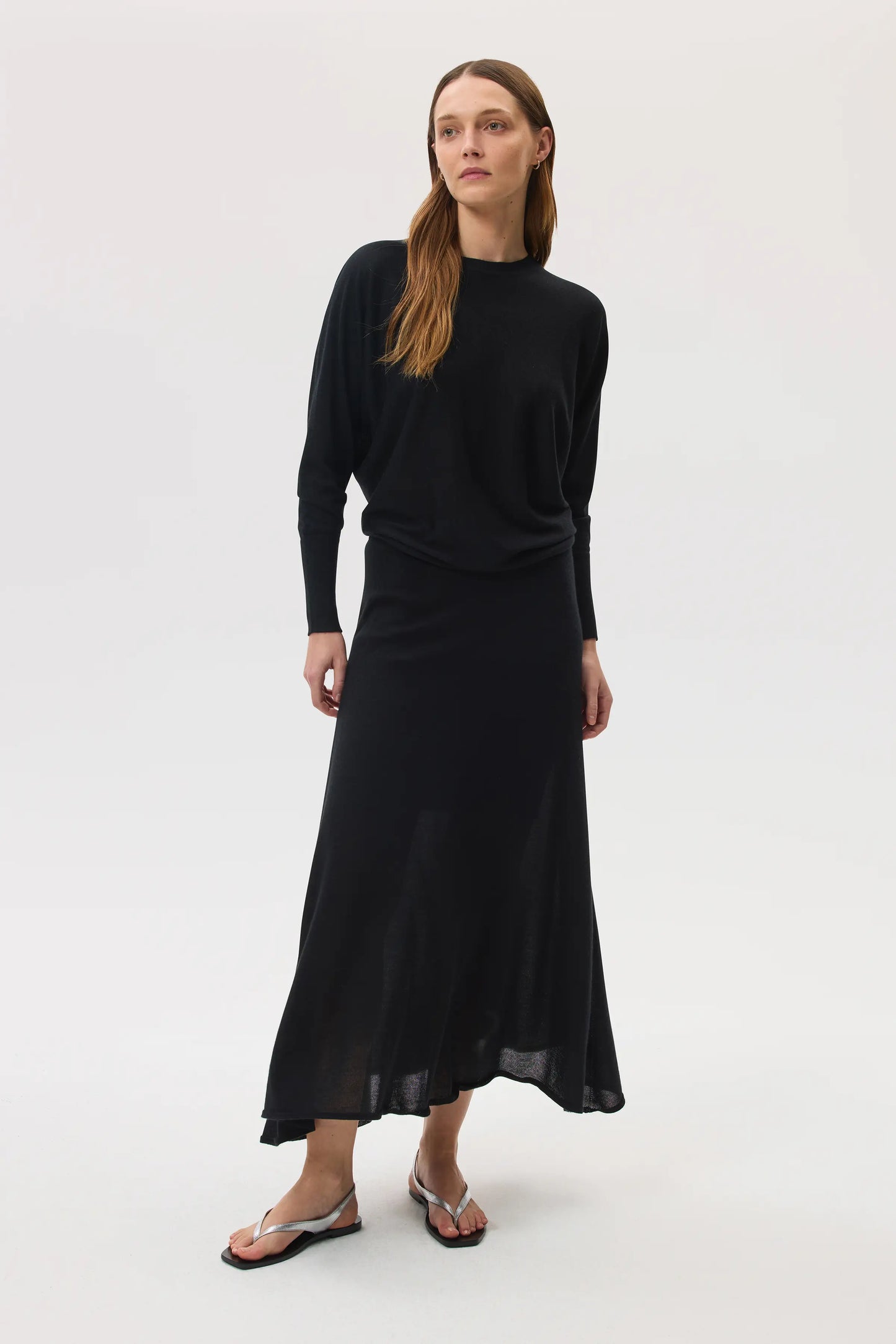 Model wears Johnstons of Elgin SS25 Women's Knitwear Black Cashmere Silk Batwing Jumper with matching black skirt on a white backdrop KBI00975SA0900