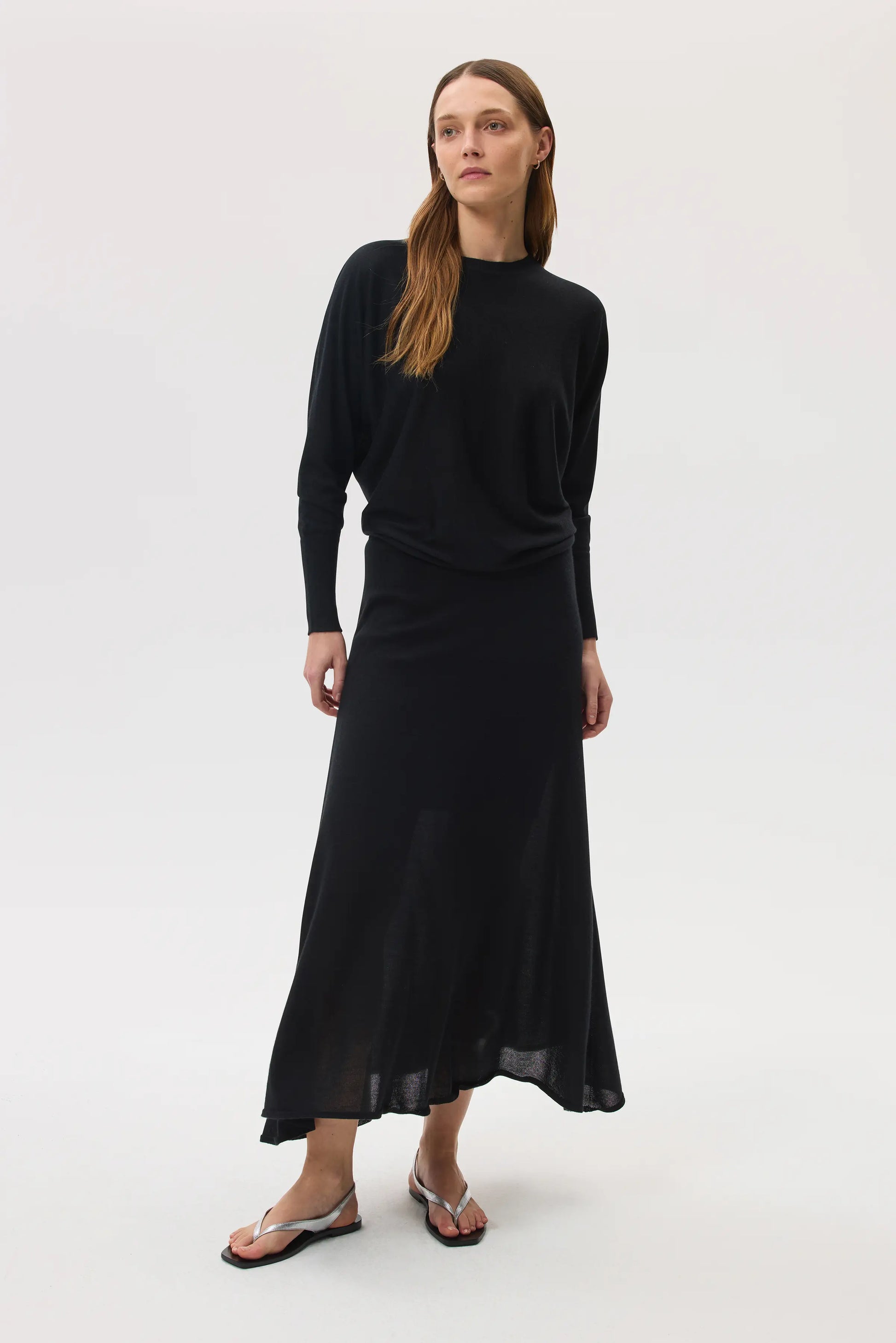Model wears Johnstons of Elgin SS25 Women's Knitwear Black Cashmere Silk Batwing Jumper with matching black skirt on a white backdrop KBI00975SA0900