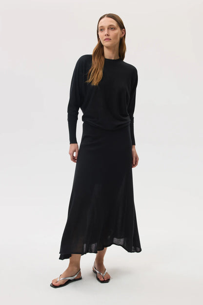 Model wears Johnstons of Elgin SS25 Women's Knitwear Black Cashmere Silk Batwing Jumper with matching black skirt on a white backdrop KBI00975SA0900