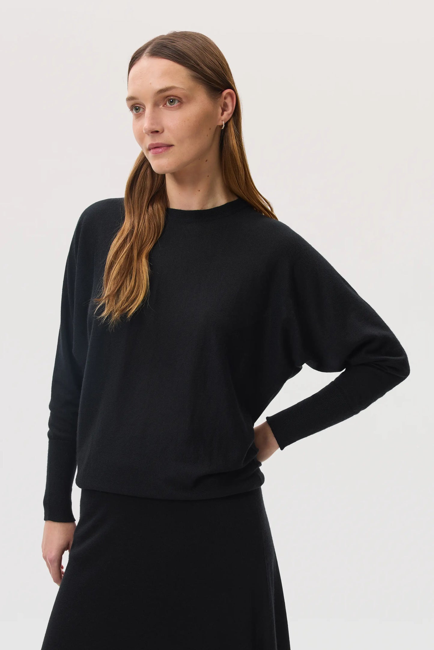 Model wears Johnstons of Elgin SS25 Women's Knitwear Black Cashmere Silk Batwing Jumper with matching black skirt KBI00975SA0900