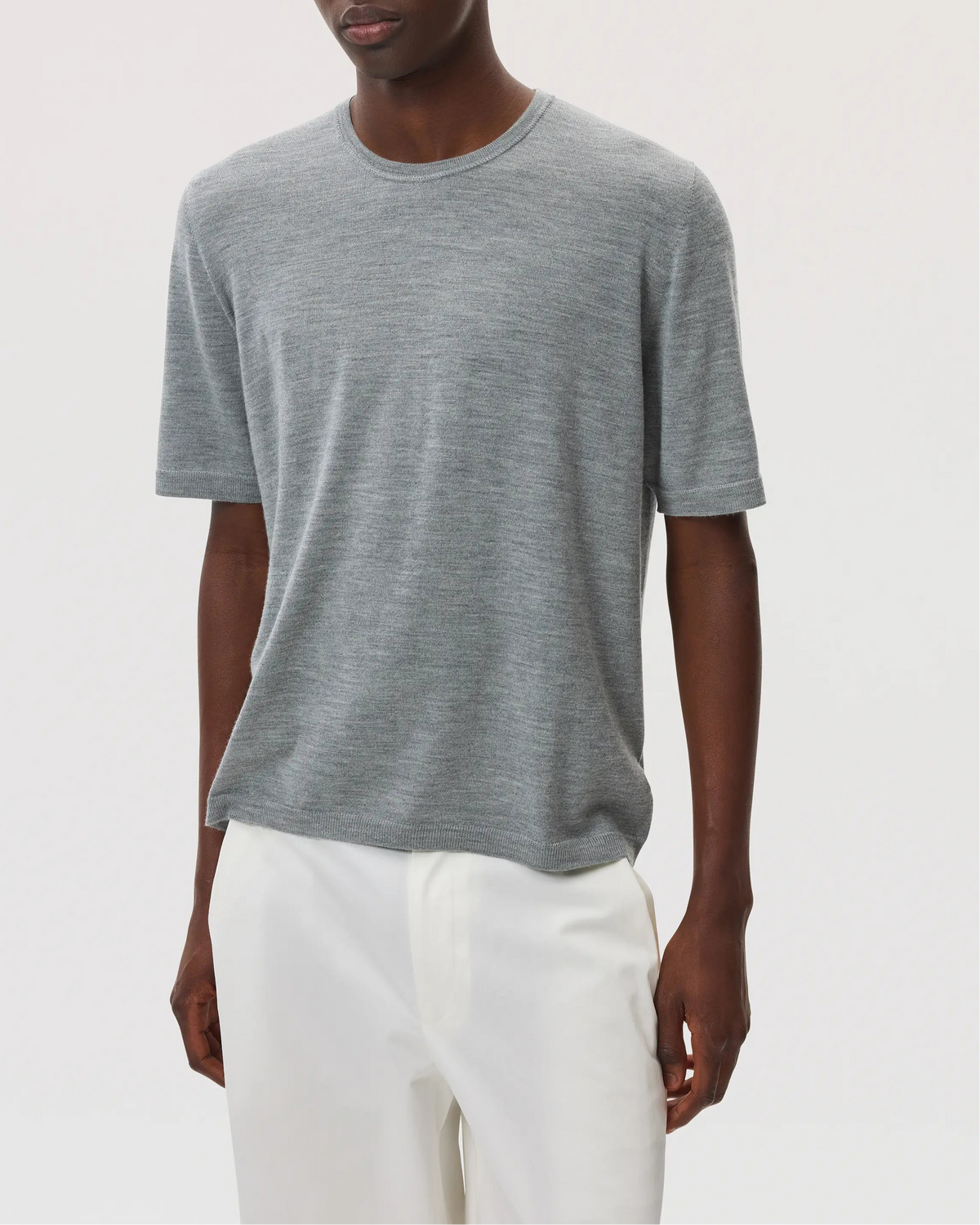 Model wears Johnstons of Elgin SS25 Men's Knitwear Light Grey Superfine Merino T-Shirt with white trousers KDI00663HA4183