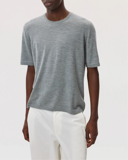 Model wears Johnstons of Elgin SS25 Men's Knitwear Light Grey Superfine Merino T-Shirt with white trousers KDI00663HA4183