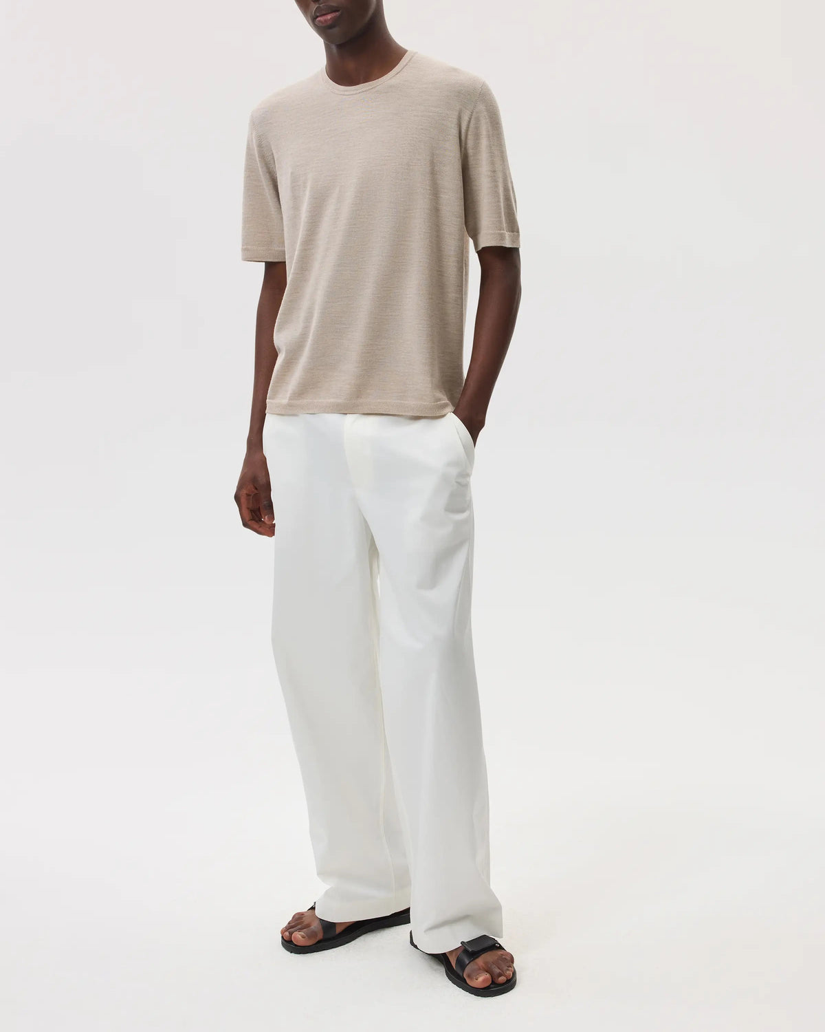 Model wears Johnstons of Elgin SS25 Men's Knitwear Natural Superfine Merino T-Shirt with white trousers and black sandals KDI00663SB0695