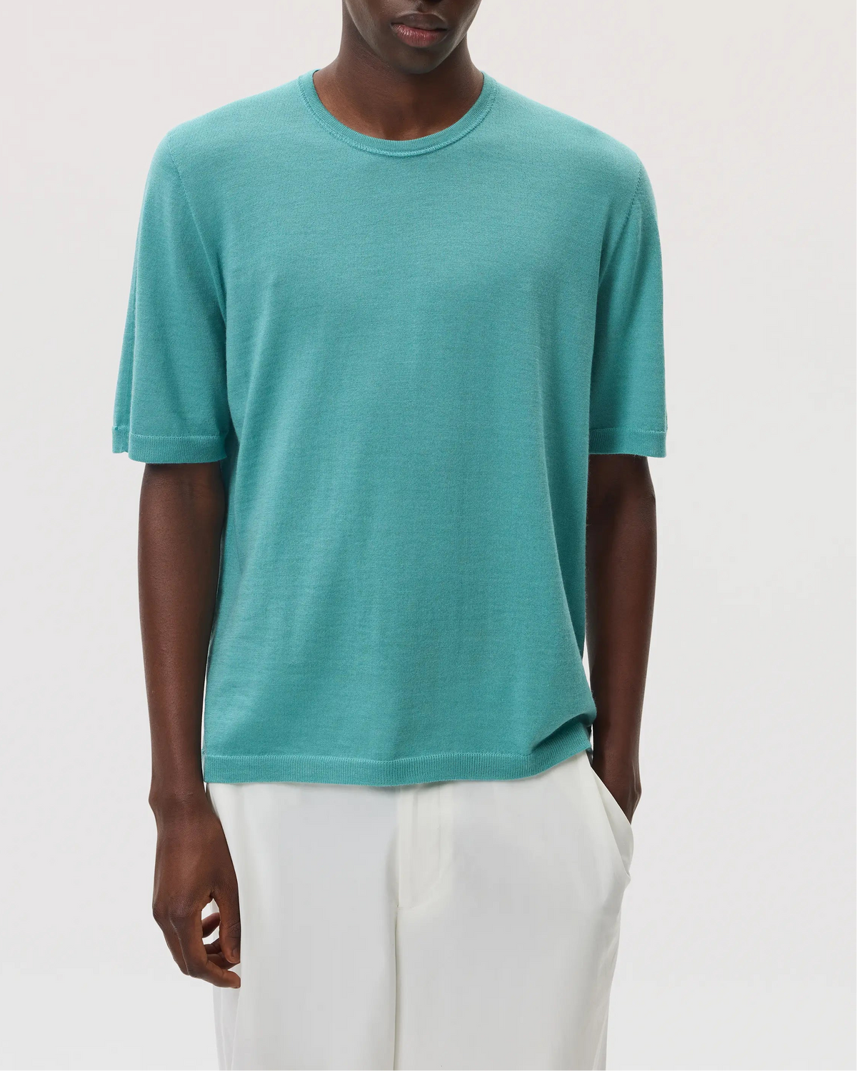 Model wearing Johnstons of Elgin SS25 Men's Knitwear Jade Superfine Merino T-Shirt with white trousers  KDI00663SC4641