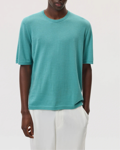 Model wearing Johnstons of Elgin SS25 Men's Knitwear Jade Superfine Merino T-Shirt with white trousers  KDI00663SC4641