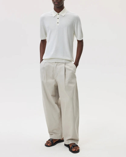 Male model wearing Johnstons of Elgin SS25 Men's Knitwear White Superfine Merino Polo Shirt with beige chinos on a white backdrop KDI00715SA0396