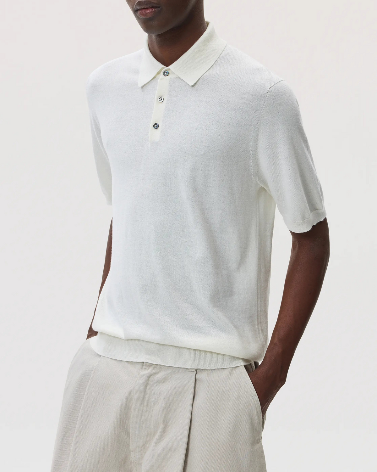 Male model wearing Johnstons of Elgin SS25 Men's Knitwear White Superfine Merino Polo Shirt with beige chinos  KDI00715SA0396
