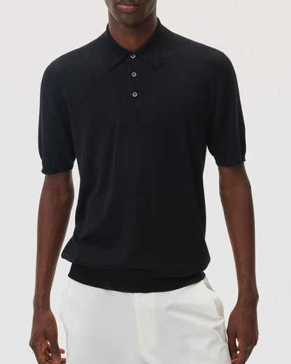Model wears Johnstons of Elgin SS25 Men's Knitwear Black Superfine Merino Polo Shirt with white trousers  KDI00715SA7131