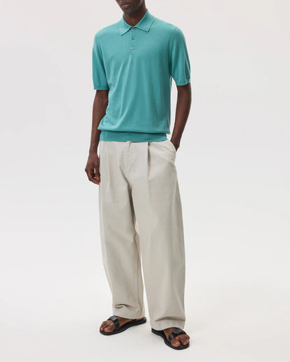 Model wearing Johnstons of Elgin SS25 Men's Knitwear Jade Superfine Merino Polo Shirt with beige chinos on a white backdrop KDI00715SC4641