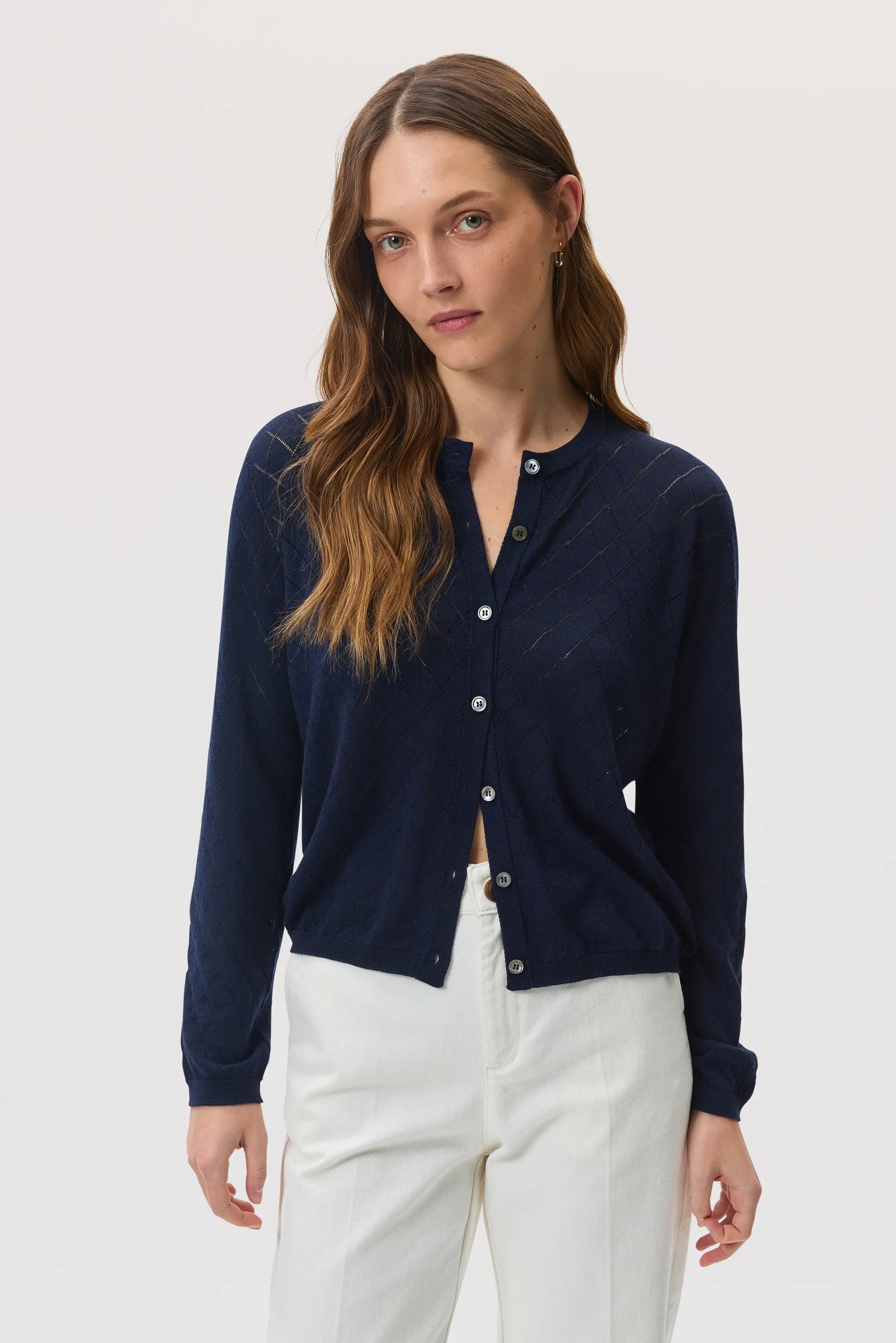 Model wears Johnstons of Elgin SS25 Women's Knitwear Navy Superfine Merino Pointelle Argyle Cardigan with white trousers KDI00742SD7563