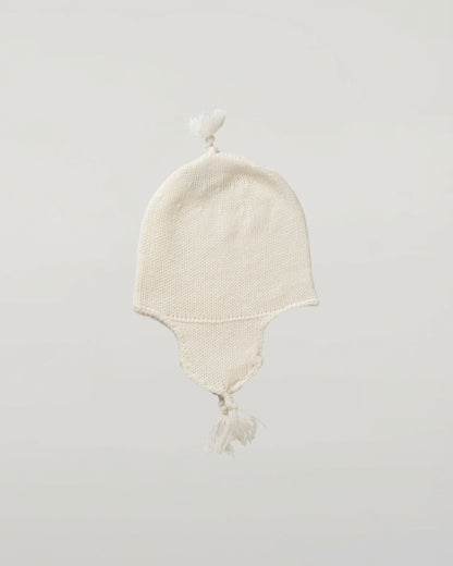 An off-white knit baby hat with ear flaps and tassels, photographed against a neutral light gray Johnstons of Elgin Baby Handknits Ecru Cashmere Baby Hat with Tassel JA000139SA0132ONE