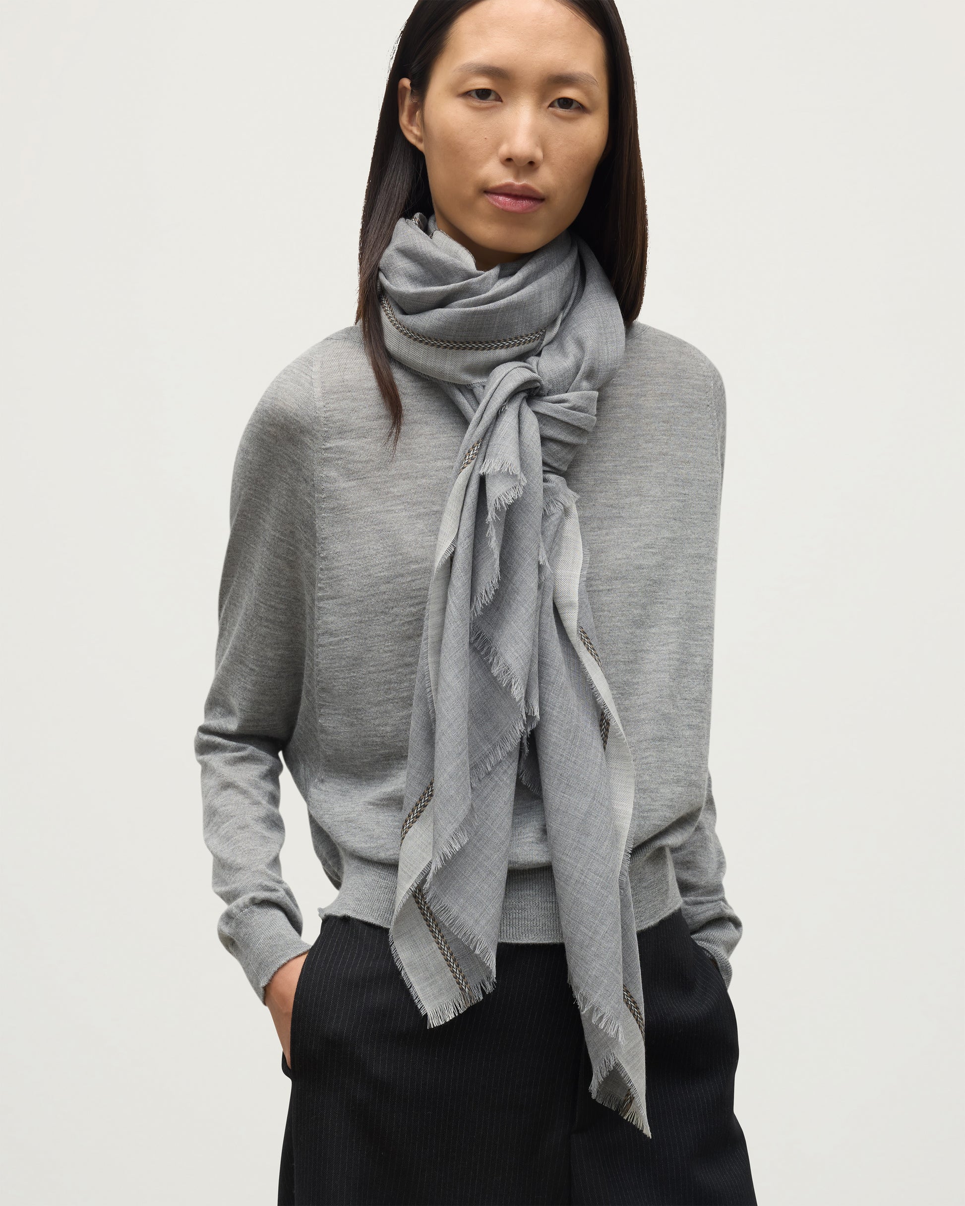 MODEL WEARS JOHNSTON OF ELGIN IVES CHEVRON BORDER SCARF 100% CASHMERE OVER A LIGHT GREY CASHMERE SWEATER WA002446RU7700ONE