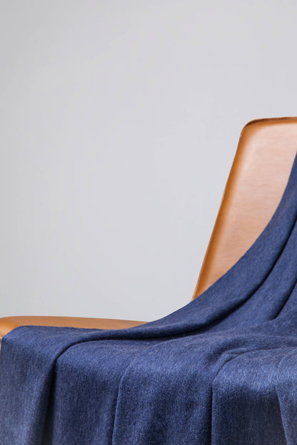 Johnstons of Elgin’s Denim Blue Cashmere Throw on brown chair on a grey background WA000055HD0724